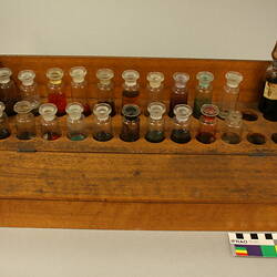 Wooden rack with twenty-one stoppered bottles containing various coloured liquids