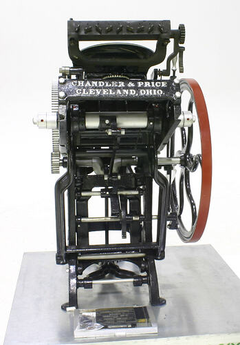 Black mechanical printing press with red flywheel.