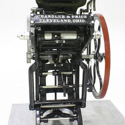 Black mechanical printing press with red flywheel.