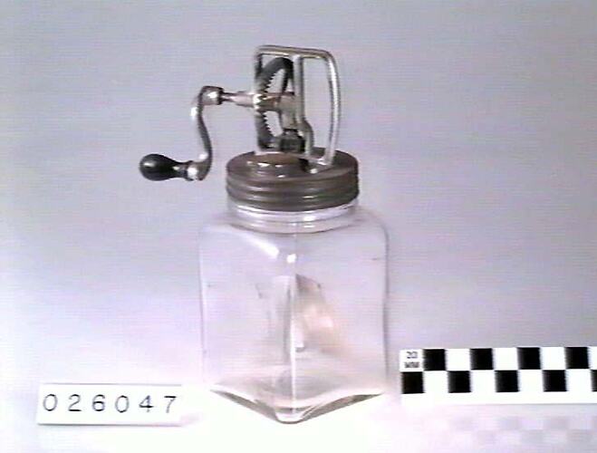 Square glass jar fitted with a hand cranked metal paddle.