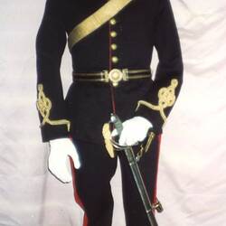 Mannequin wearing black military uniform with white helmet and sword, front view.