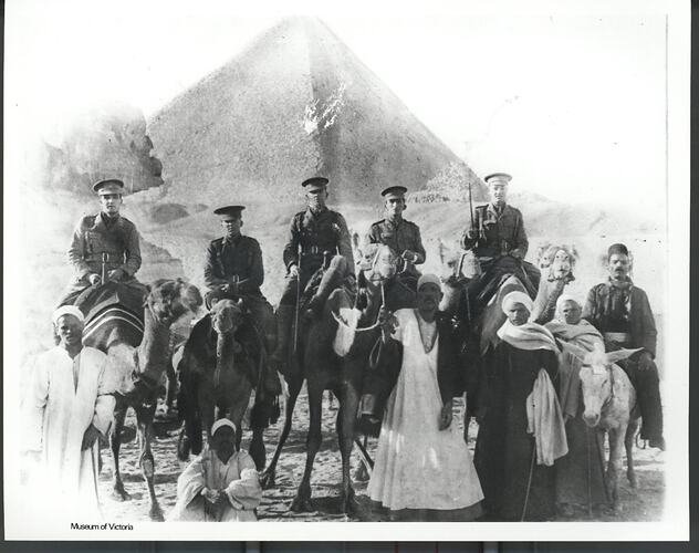 Five army officers on camels in front of a pyramid.