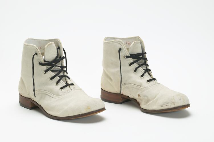 Pair of cream canvas ankle high boots with black laces.