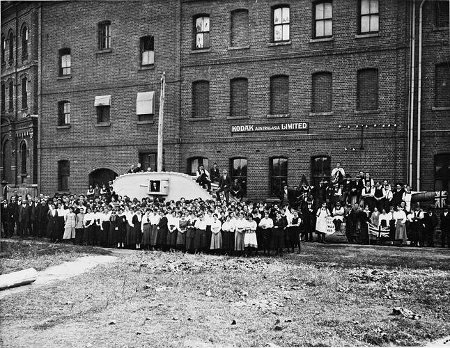 Group photo of Kodak staff outside the Abbotsford factory during a war bonds appeal. A tank can be seen parked in the background.