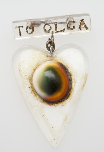 White heart pendant with central dark circle. Hangs from badge with text.