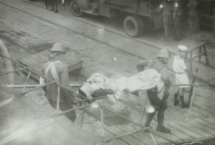 Two men walking a stretcher with an injured person down a gangway.