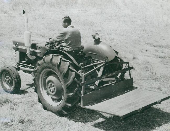 Rear view of a man driving a tractor with a Transporter attached, across a field.