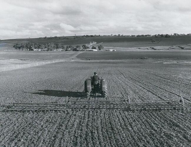 Rear view of a harrow being towed by a tractor across wide open field.