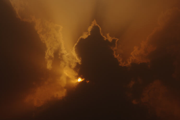 Dark orange and yellow sun rays sun shine through dark smoke and clouds.