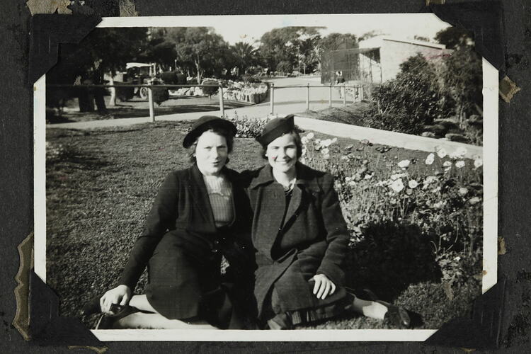 Two woman sitting on grass in garden.