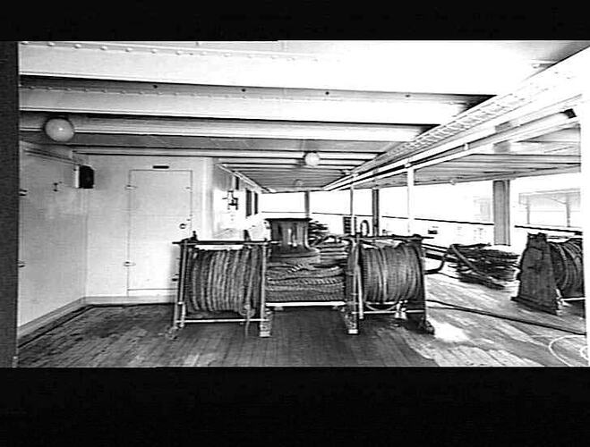 View of covered ship deck with capstan and large wire hawser reels.