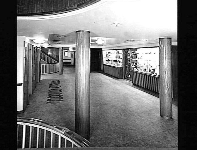 Ship interior. Entrance area with pillars. Shelving section at right and a staircase in background.