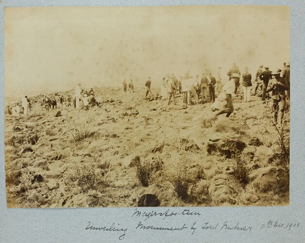 Grassy field with group of people standing facing away from camera.