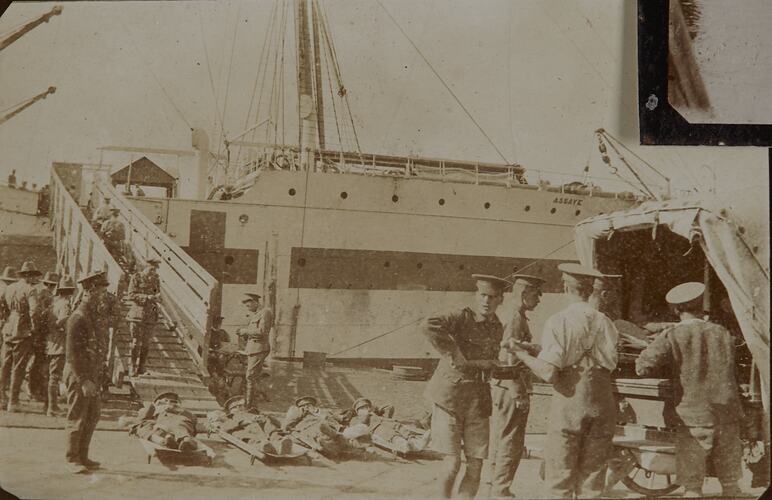 Loading wounded soldiers on stretchers laid on ground onto Hospital Ship. Horsedrawn ambulance at right.