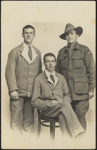 Three men, two standing and one seated in front.