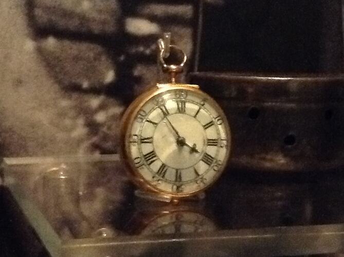Gold pocket watch in display cabinet.