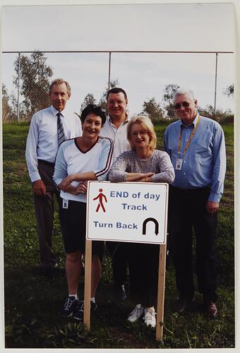 Two women and three men posing behind a sign.