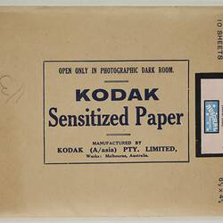 Flat sealed rectangular paper envelope with dark blue inscription. Pink sticker secures the flap.