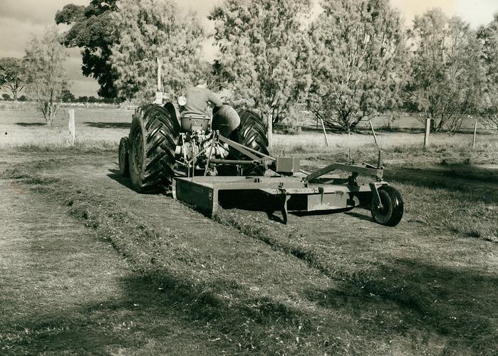 A man driving tractor coupled to a rotary slasher.