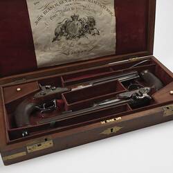 Two guns in wooden case, burgundy lining. Has seven sections. Label in lid.
