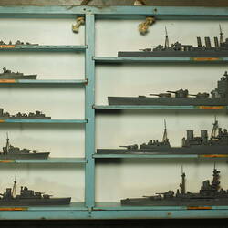 Blue and grey wooden case holding 9 grey ship models in two columns.