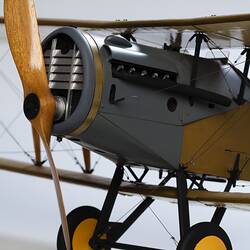 Model biplane aeroplane painted mustard brown with grey engine. Three quarter right view, engine and propeller