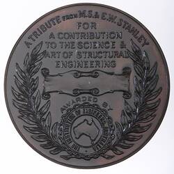 Round medal with raised text, blank scroll and Australia logo framed by wreath.