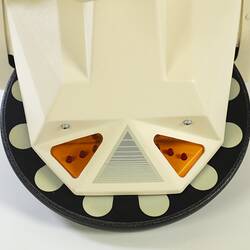 Detail of base of cream plastic robot with angular human-like shape, ie. head, shoulders, waist and legs. Black plastic features.