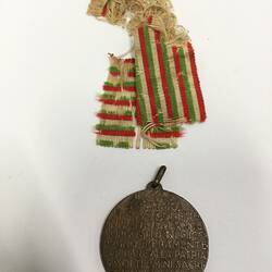 Round dark medal with separate frayed green, red and white striped ribbon.