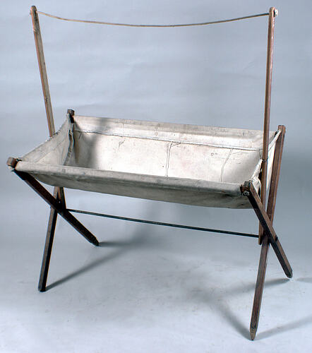 Side view of wood and cloth bassinet.