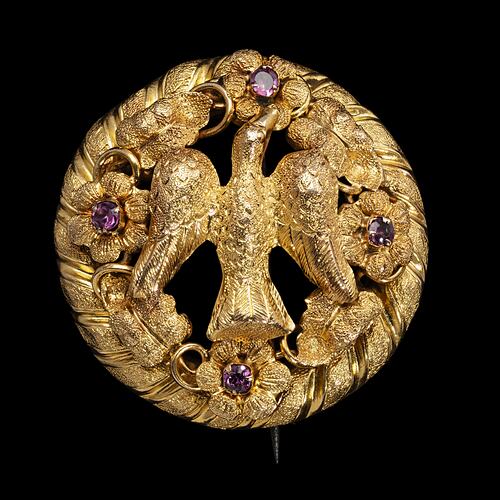 Round gold brooch with large bird and four purple paste stones.