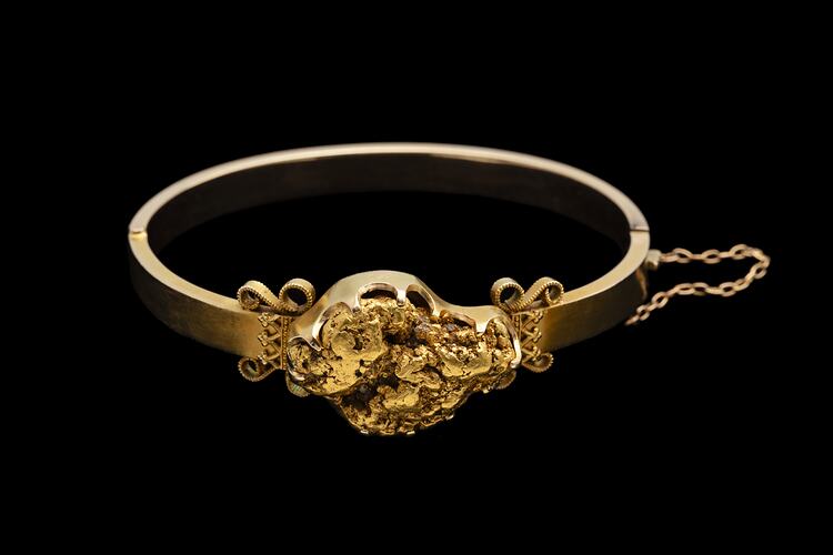 Gold bangle (bracelet) featuring a large gold nugget. Fine chain at right side.