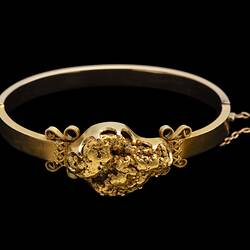 Gold bangle (bracelet) featuring a large gold nugget. Fine chain at right side.