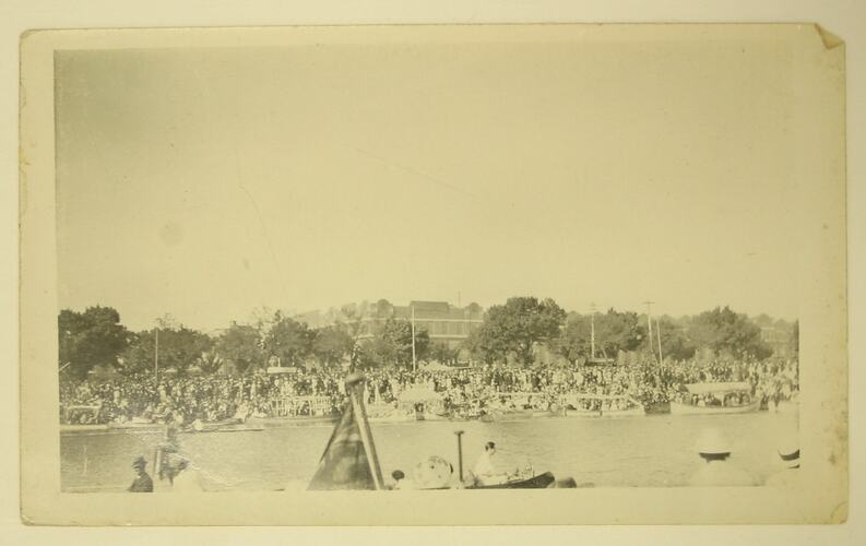 Crowds on bank watching a boating event.
