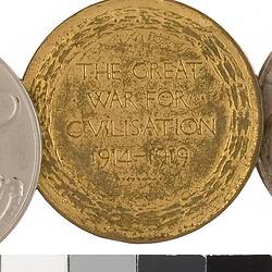 Round gold coloured medal with text in centre, surrounded by wreath, with rainbow coloured ribbon.
