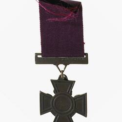 Cross shaped medal with engraving in centre. Burgundy ribbon.