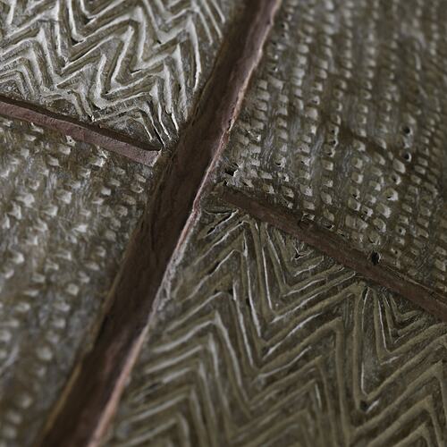 Detail of incised decorations on a wooden shield.