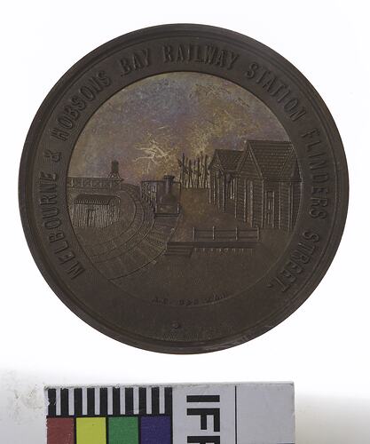 Round medal with railway yard scene, text around.