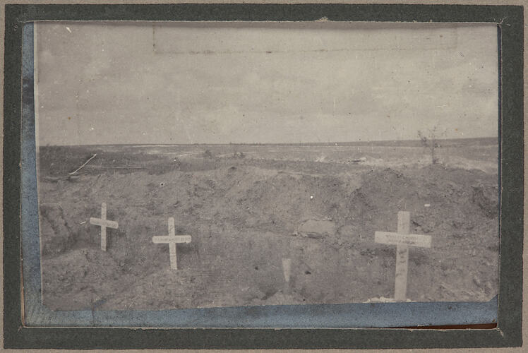 Three graves with cross shaped markers and mound of dirt behind.