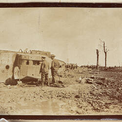 Tank in mud with servicemen and barren landscape behind.