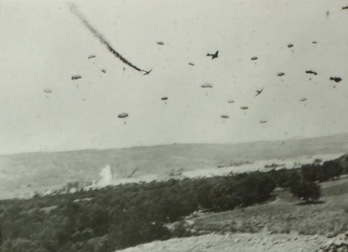 Large group of parachuters and plains in the air, with ground below.