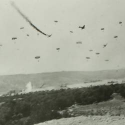 Large group of parachuters and plains in the air, with ground below.