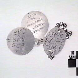 Two circular and one oval shaped disc with inscribed text and metal chain attached.