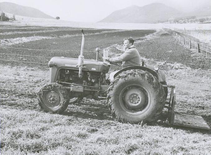 Side view of a man driving a tractor with a Transporter attached, across a field.