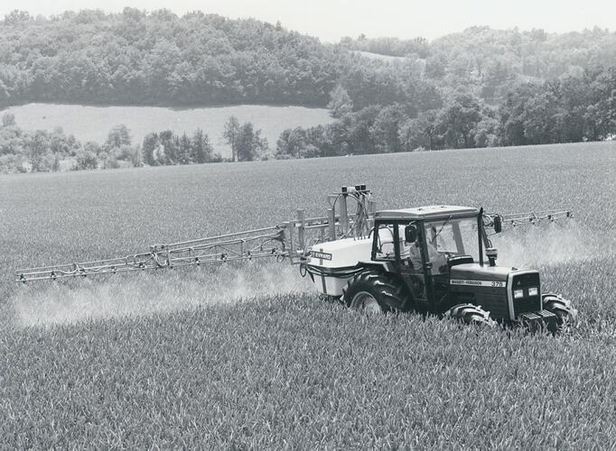 Tractor fitted with spray boom in grain crop.