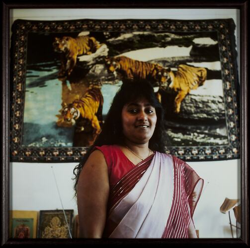 Woman wearing red and white sari stands in front of tiger wall hanging.