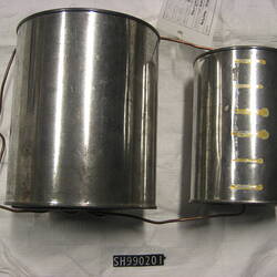 Two silver metal tins. Wire joins them via holes in each lid and base making a handle at the front larger tin.