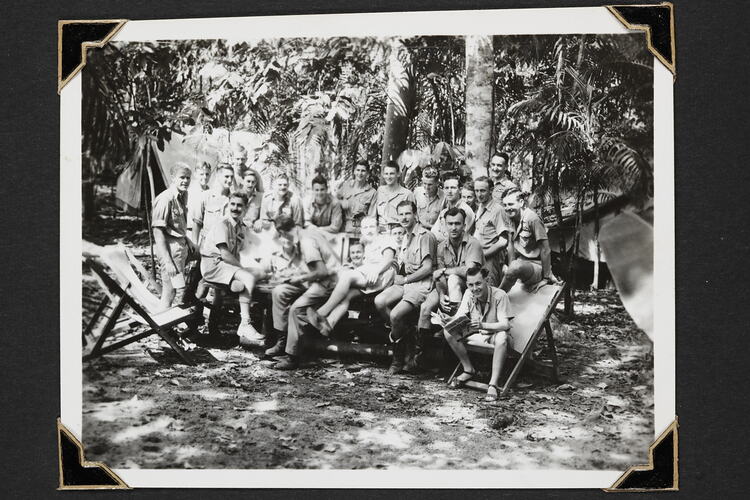 Group of men sitting on a table outside with trees and foliage behind.