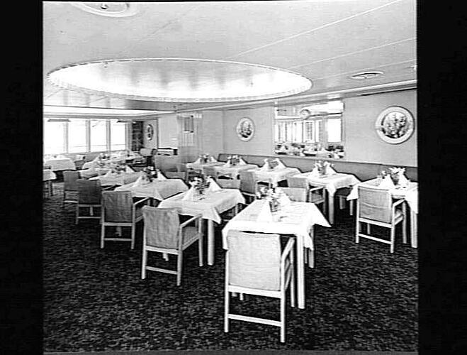 Ship interior. Dining room with chairs and tables. Tablecloths and flower vases decorate each table.