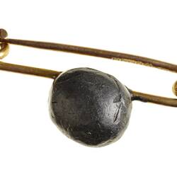 Gold pin brooch with small lead bullet mounted on it.